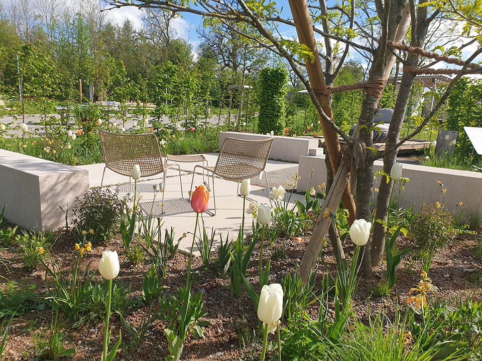 Sitzplatz im Garten umgeben von Grün, Tulpen und anderen Pflanzen