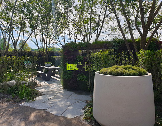 Garten mit großem Blumenkübel und einer Sitzmöglichkeit im Hintergrund