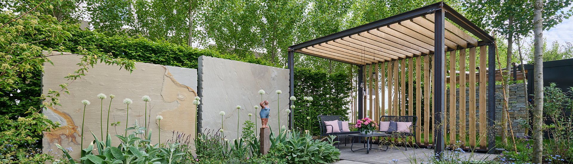 Pergola mit Sitzplatz und einer Natursteinmauer als Sichtschutz