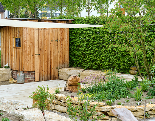 Garten mit kleinem Holzhaus, Steinmauer mit Beet